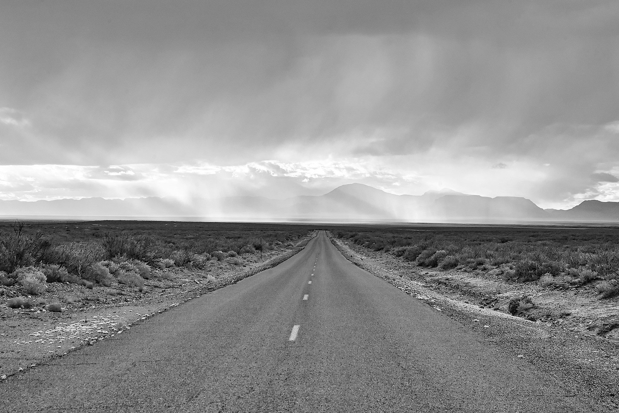 Narrow desert road with a distant storm approaching over Tularosa Basin, New Mexico